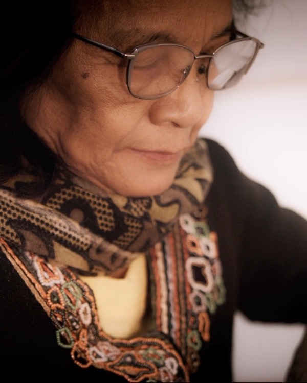 A frame from A Handful of Rice: an intimate close-up of a grandmother in wire-rimmed glasses looking down at her work
